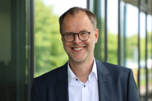 Das Bild zeigt Herrn Prof. Dr. Bernd Kriegesmann im Porträt. Er lächelt und trägt ein dunkelblaues Sakko über einem weißen Hemd. Der Bildhintergrund ist unscharf.