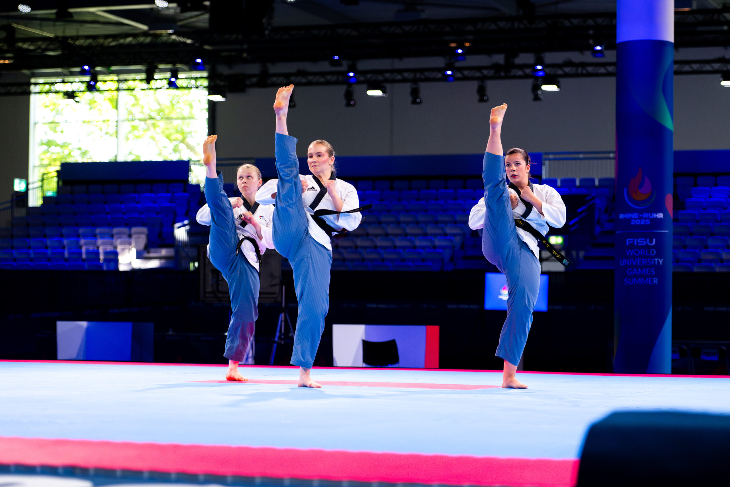 Drei Frauen sind auf der Matte im typischen Taekwondo-Anzug. Ihr jeweiliges rechtes Bein ist weit in die Höhe gestreckt. Die Hände sind vor dem Körper zu Fäusten geballt. Foto: adh/ Jan Patrick Wagner