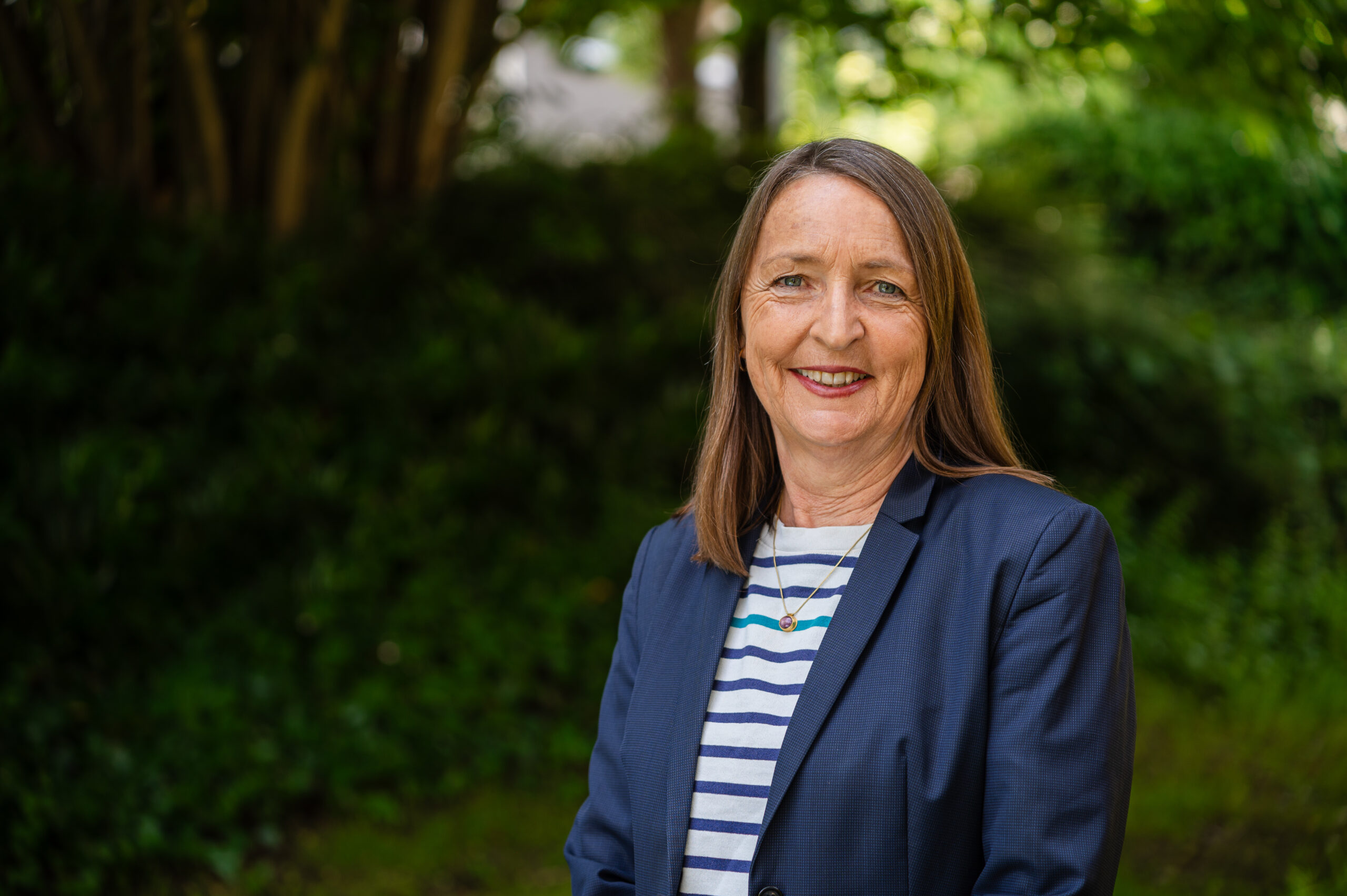 Auf dem Bild ist Prof. Dr. Dr. Sigrid Graumann im Porträt zu sehen. Im Hintergrund sind Bäume, Büsche und viel Grün zu sehen.